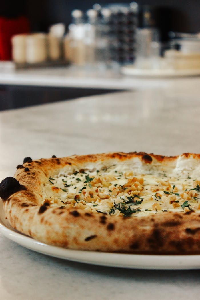 Close-up of a gourmet pizza topped with herbs and nuts on a marble counter.